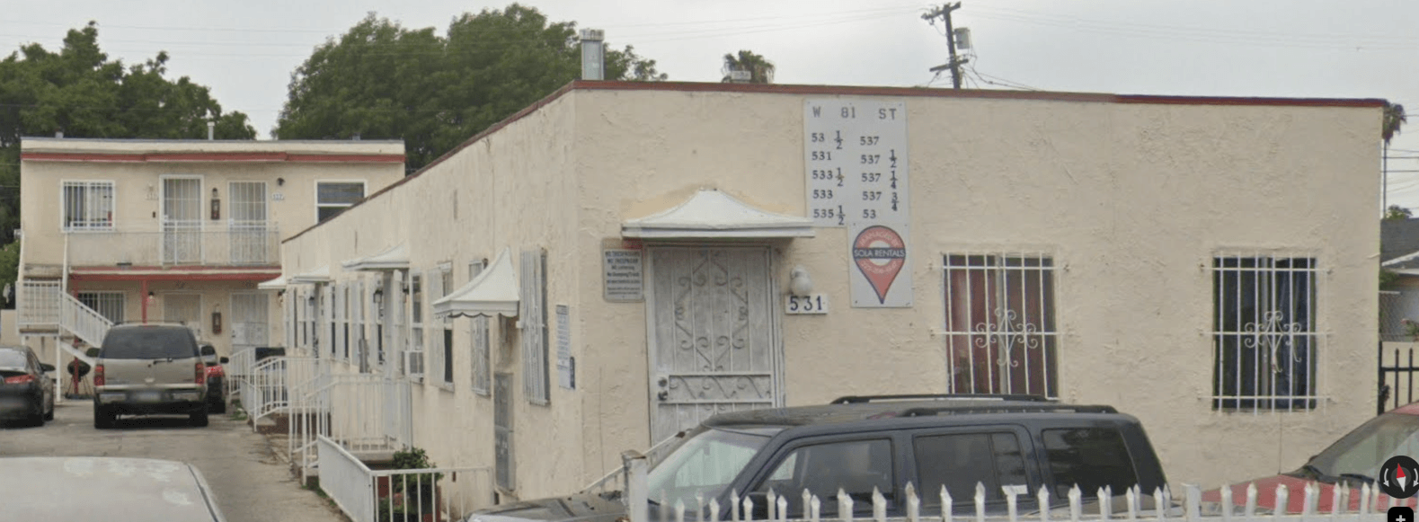 A white building with a sign on it and a car parked in front.
